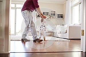 Father helping daughter learn to walk at home, side view