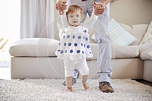 Father helping daughter learn to walk in the sitting room