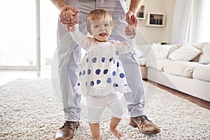 Father helping daughter learn to walk in the sitting room