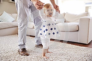 Father helping daughter learn to walk in the sitting room