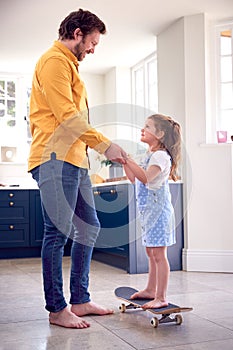 Father Helping Daughter To Balance On Skateboard Indoors At Home