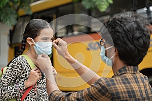 Father helping daughter to wear mask before getting inside the school bus as coronavirus or covid-19 safety measures - concept of