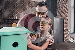 Father helping daughter use drill to make birdhouse in the