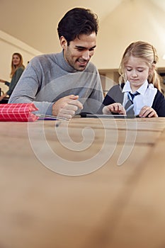 Father Helping Daughter Using Digital Tablet Wearing School Uniform With Homework At Table