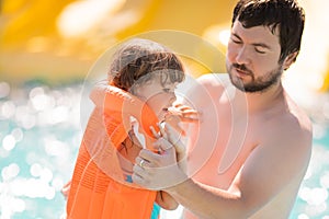 Father helping his cute toddler daughter wuth her life jacket in outdoors swimming pool in water park aquapark