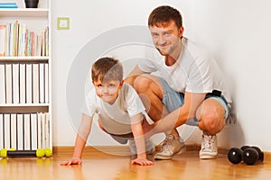 Father helping his kid son doing press-ups at home