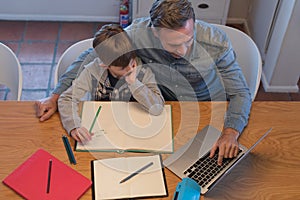 Father helping his son with his homework while using laptop
