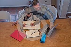 Father helping his son with his homework while using laptop