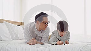 Father is helping his son on school homework on a bed at home.