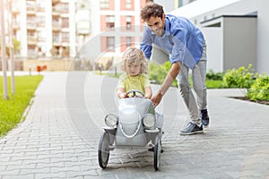 Father helping his son to drive a toy peddle car