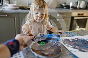Father helping little girl painting with tempera paint using a paintbrush.