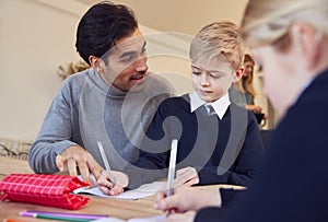 Father Helping Son And Daughter Wearing School Uniform With Homework At Table In Kitchen