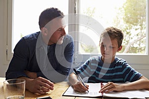 Father Helping Son With Homework Sitting At Kitchen Table