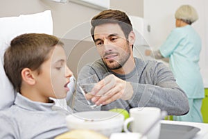 father helping son in hospital bed to drink water photo