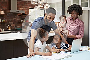 Father Helps Children With Homework Whilst Mother Holds Baby