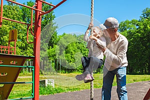 Father helps his child`s daughter to climb the rope. Concept of helping young people