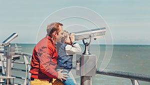Father helps his little son to look in sea binoculars
