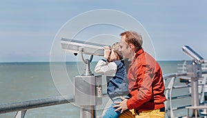 Father helps his little son to look in sea binoculars