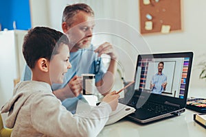 Father helps his son with home work. Boy in video conference with teacher on laptop at home