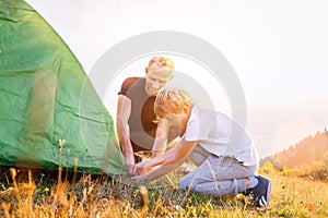 Father helps his son setting tent on sunset forest glade