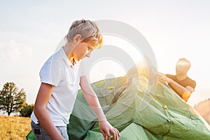 Father helps his son setting tent on sunset forest glade