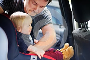 Father helps his son to fasten belt on car seat