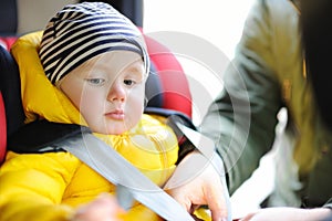 Father helps his toddler son to fasten belt on car seat