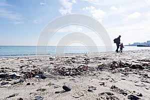 Father with his baby are walking at the trashed beach.