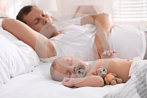 Father with his cute baby sleeping in bed at home