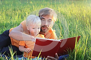 Father and his cute toddler son read book together in nature. Authentic lifestyle image. Parenting concept photo