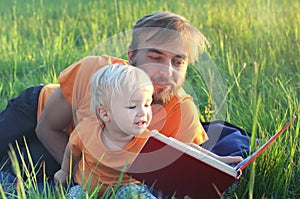 Father and his cute toddler son read book together outdoor. Authentic lifestyle image. Parenting or childhood concept