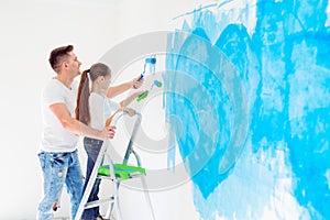 Father and his little daughter painting a wall in new home.