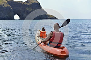 A father and his little daughter are sailing on the sea in a kayak to a grotto