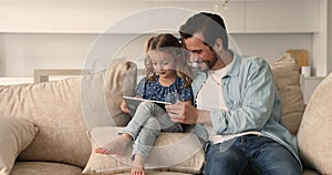 Father his little daughter sit on comfy couch using tablet