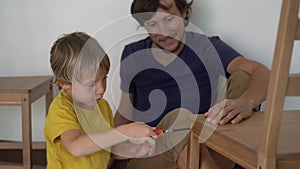 Father and his little son are assembling furniture. They assemble a kitchen chair