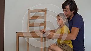 Father and his little son are assembling furniture. They assemble a kitchen chair
