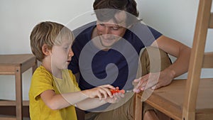 Father and his little son are assembling furniture. They assemble a kitchen chair