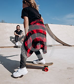 Father and his little son dressed in the casual clothes ride skateboards and have fun in a skate park with slides