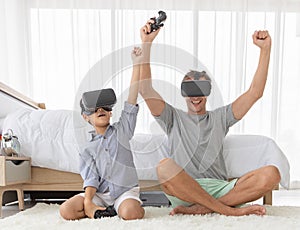 Father and his mixed-race son wearing vr virtual reality device to play a game together with fun and happy in bedroo