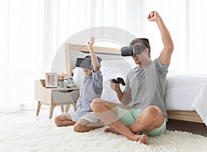 Father and his mixed-race son wearing vr virtual reality device to play a game together with fun and happy in bedroo