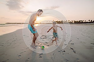 Father with his son plaing football on the beach.