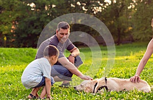 Father and his son playing with dog in park -happy family is having fun with golden retriever .