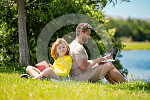 Father with his son reading book together in the summer park. Father and son having a picnic in the park, happiness