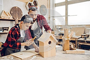 Father and his son working together in a wooden workshop, building a birdhouse