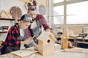 Father and his son working together in a wooden workshop, building a birdhouse photo