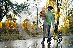 Father and his tiddler son walking in the park on good autumn day. Dad holding kid in one hand and child`s bicycle in another photo