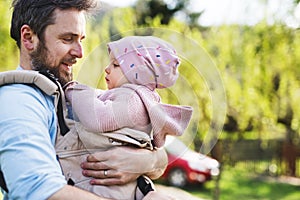 A father with his toddler daughter in a baby carrier outside on a spring walk.