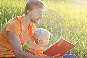 Father and his toddler son read book together outdoor. Copy cpace