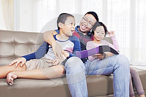 Father and his two children reading a book at home