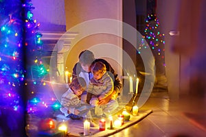 Father and his two little children sitting by fireplace chimney on Christmas Eve time. Dad and kids boys sons playing